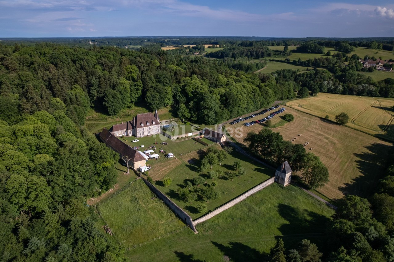Vue aérienne d'un domaine entouré de verdure avec bâtiments historiques, jardin clos et chapelle, en pleine campagne.