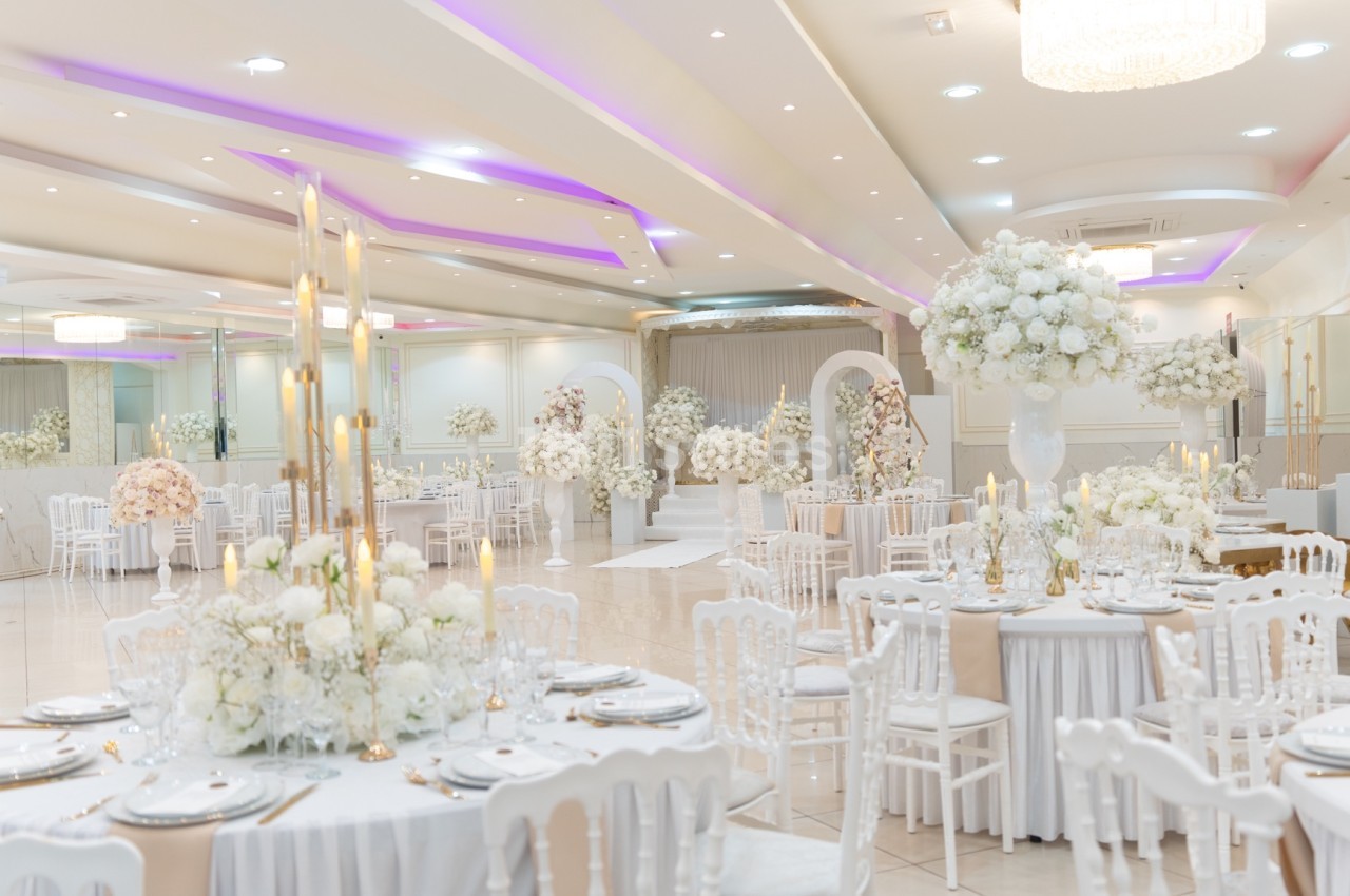 Salle de réception élégante décorée de fleurs blanches, tables dressées et éclairage tamisé.