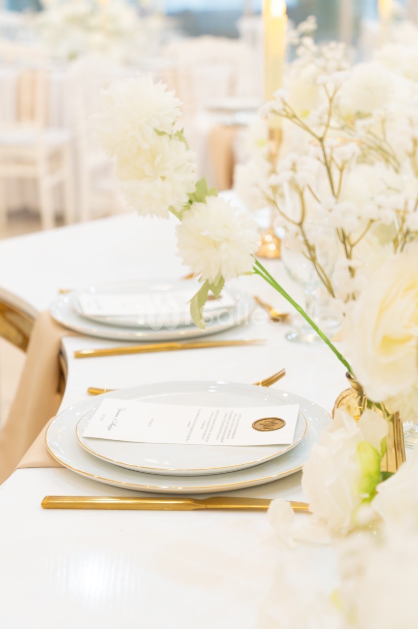 Table élégamment dressée avec vaisselle blanche, couverts dorés et décoration florale blanche.