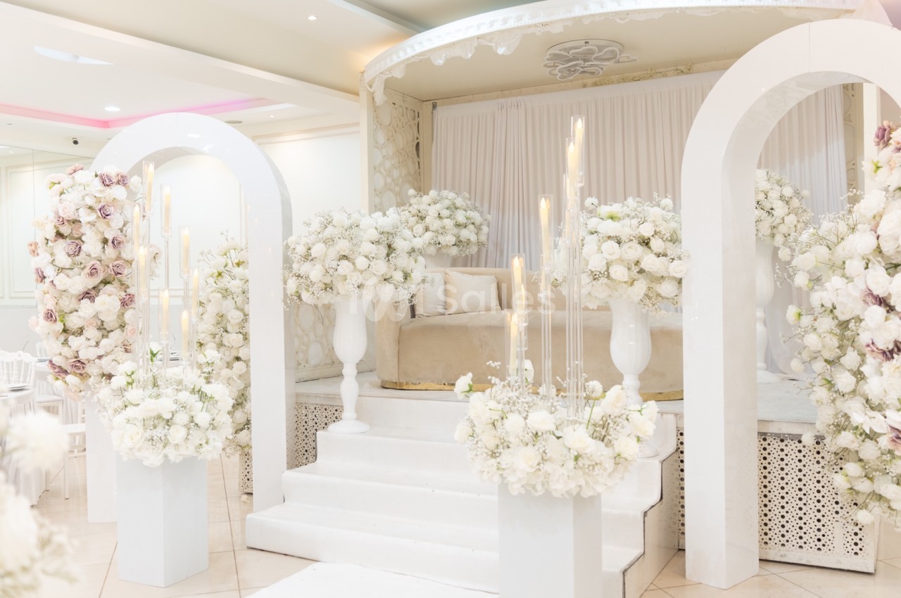 Décoration de mariage avec arche blanche, fleurs blanches et roses, et estrade ornée de bougies et rideaux.