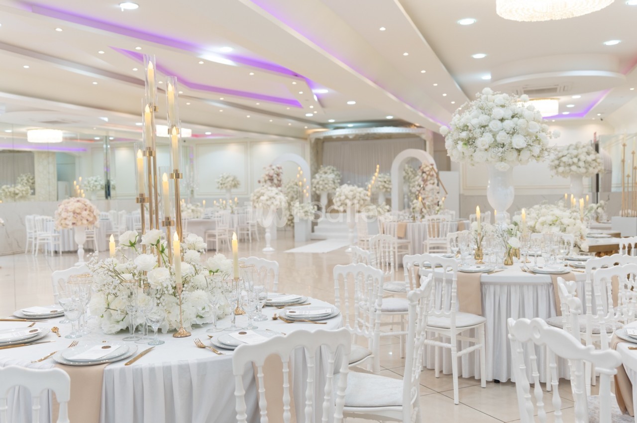 Salle de réception élégante avec tables décorées de fleurs blanches et chaises blanches, éclairage doux et arches fleuries.
