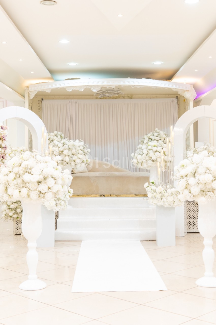 Salle de réception décorée de fleurs blanches, avec une estrade centrale et un éclairage lumineux.