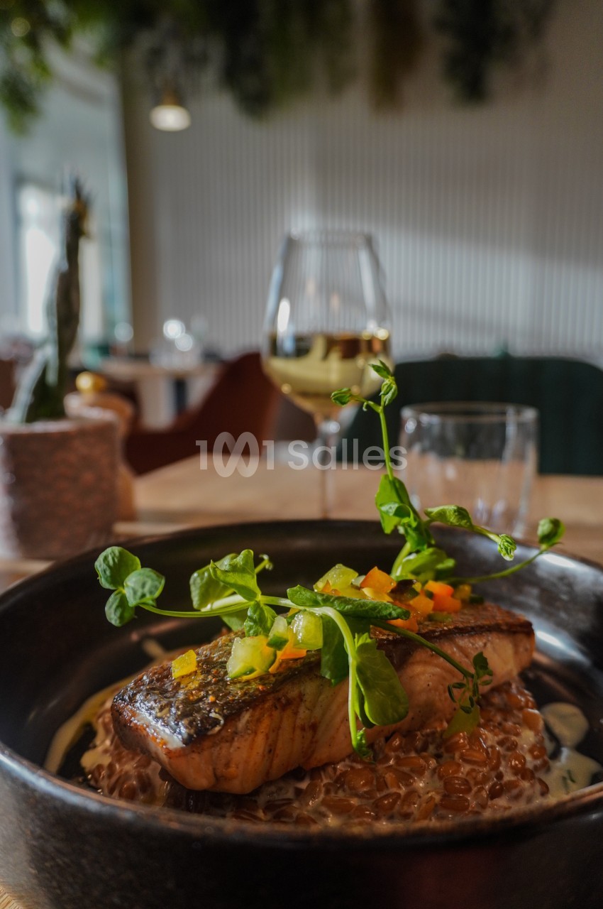 Filet de saumon grillé servi sur un lit de céréales avec des légumes colorés, dans un restaurant élégant.