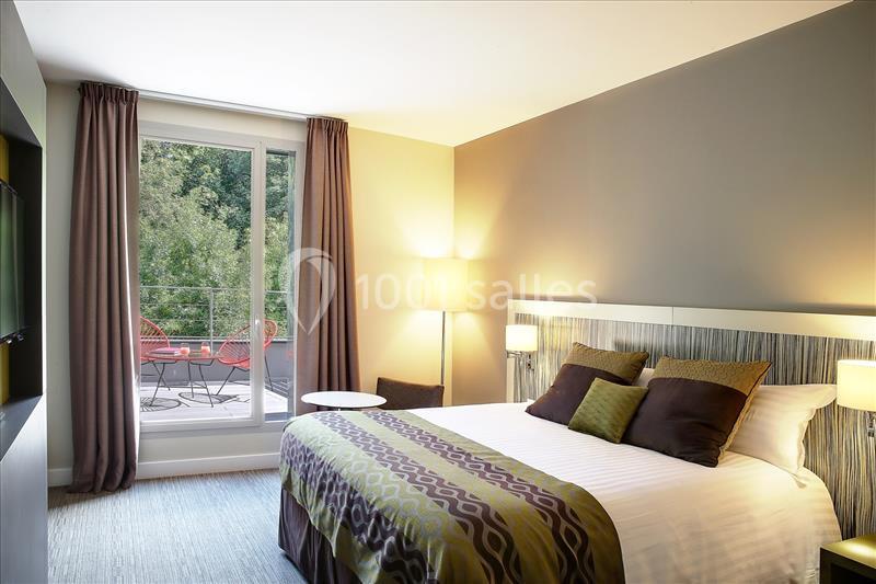 Chambre lumineuse avec lit double, décor moderne, grandes fenêtres donnant sur une terrasse avec vue sur la verdure.