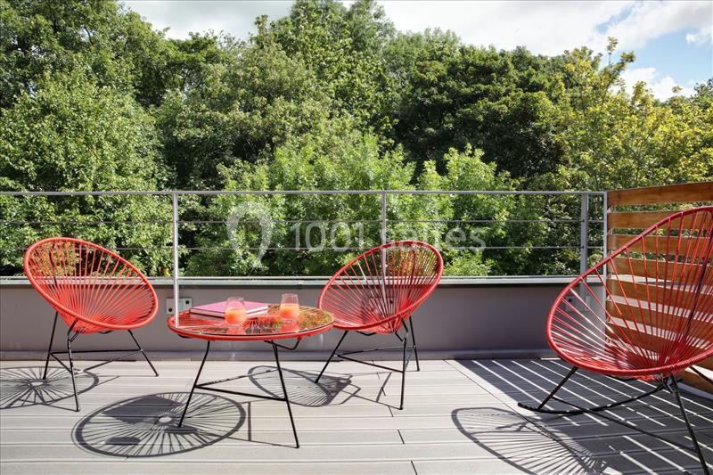 Terrasse avec mobilier rouge moderne, table basse et vue sur une végétation dense en arrière-plan.