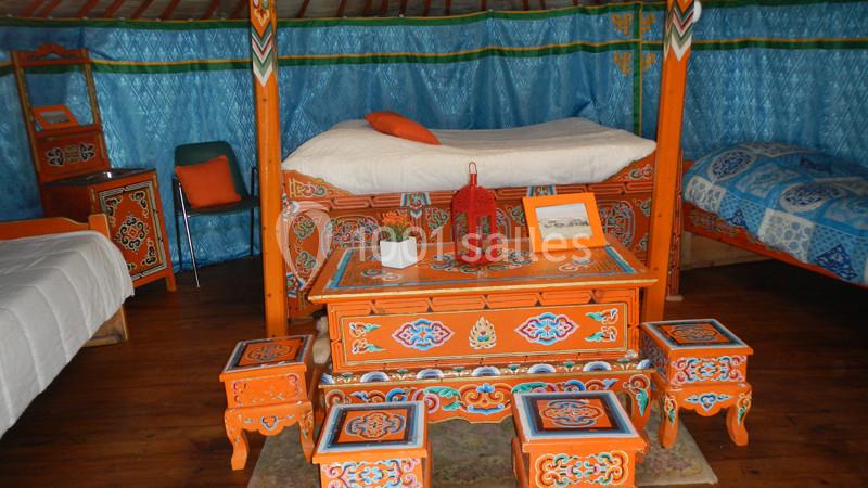 Mobilier traditionnel coloré dans une yourte, avec lits, tables et tabourets ornés de motifs décoratifs.