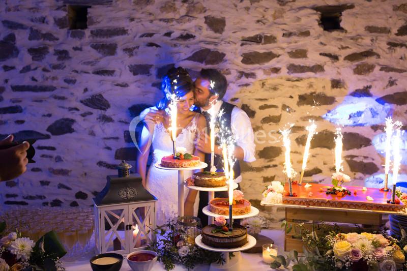 Un couple de mariés souffle des bougies sur des gâteaux décorés, entourés de lumières et d'une table festive.