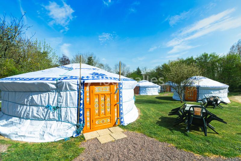 Trois yourtes blanches avec portes décorées en orange, installées sur une pelouse entourée d'arbres sous un ciel bleu.
