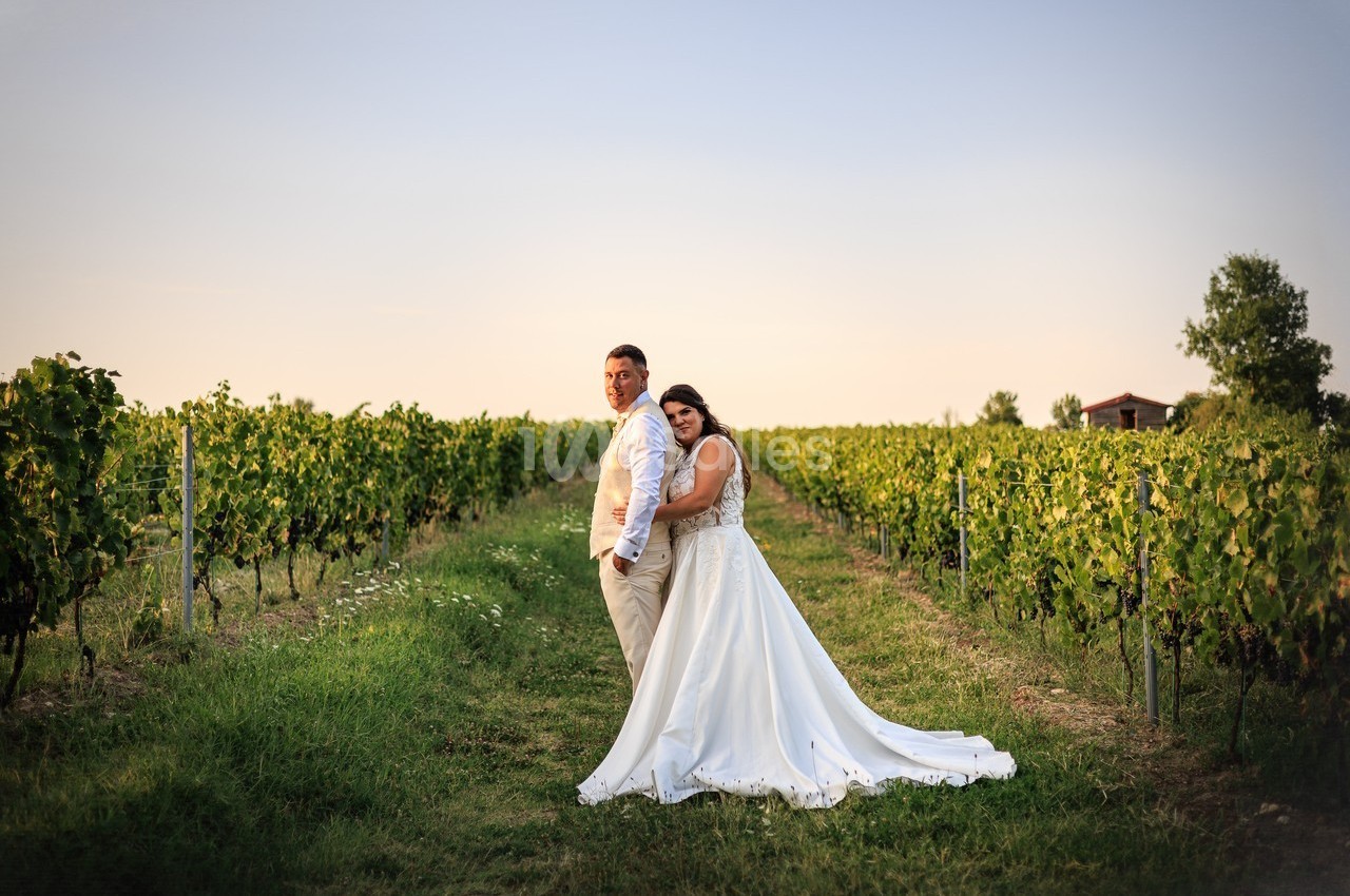 Un couple en tenue de mariage pose dans un vignoble au coucher du soleil.