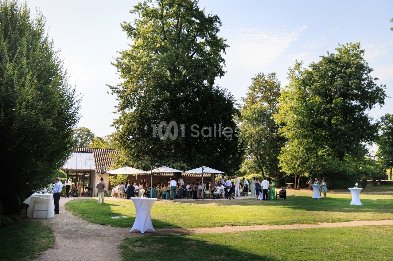 Groupe de personnes réunies dans un jardin avec tables, parasols et arbres en arrière-plan par une journée ensoleillée.