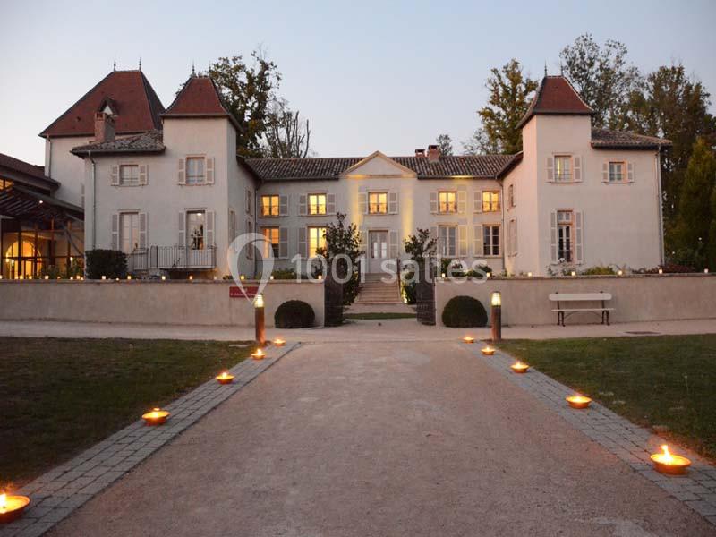 Allée éclairée menant à un grand bâtiment ancien avec des tours et des fenêtres illuminées au crépuscule.