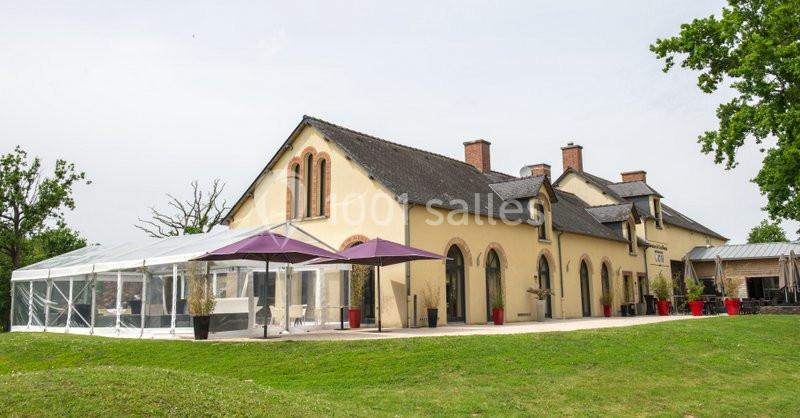Bâtiment à façade jaune avec une verrière et des parasols violets, entouré d'herbe et d'arbres.