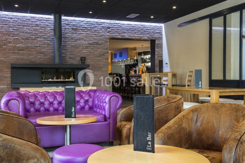 Espace lounge avec fauteuils en cuir, canapé violet, tables basses et vue sur un bar en arrière-plan.