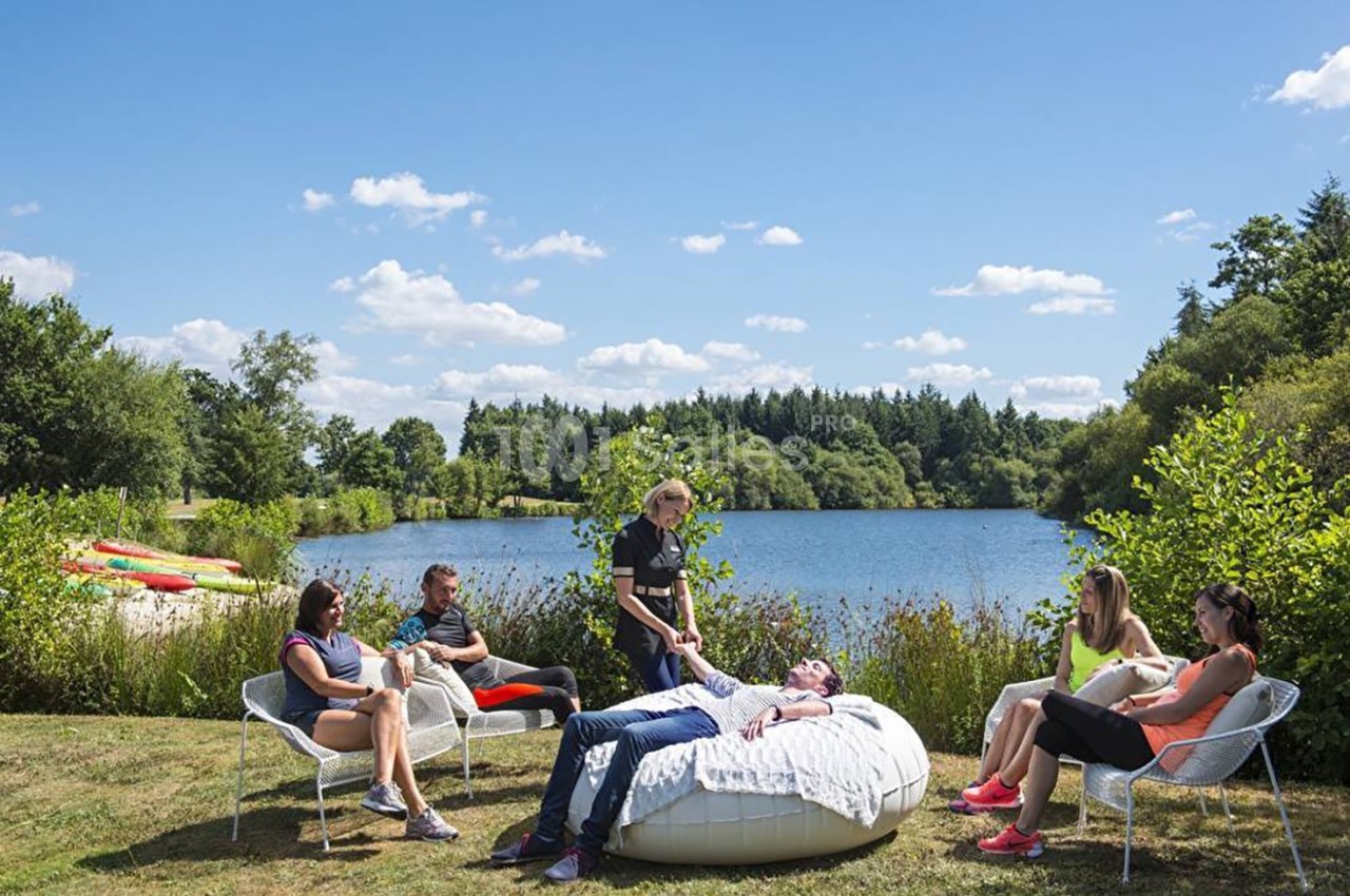 Un groupe de personnes assises près d'un lac, entouré de verdure, avec une personne allongée sur un pouf.
