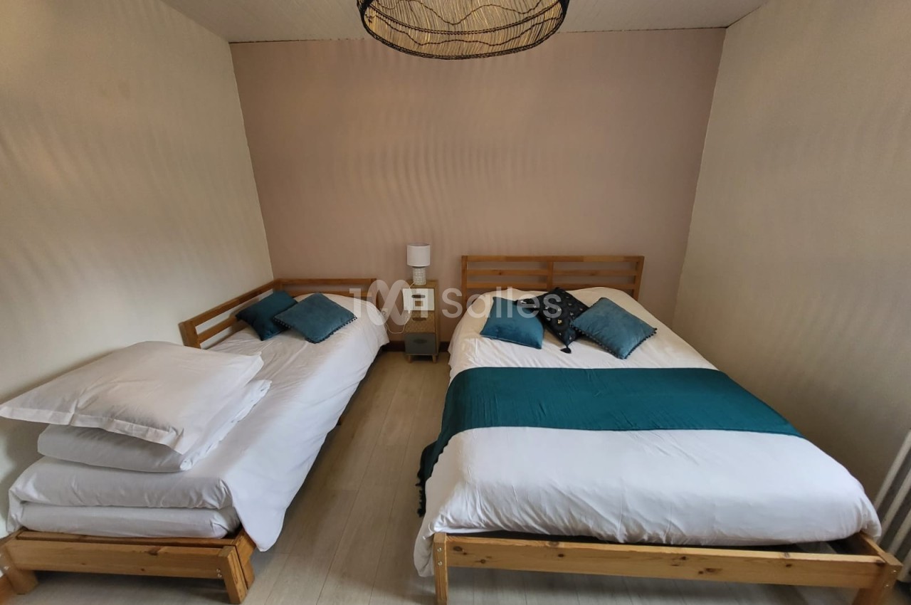 Deux lits en bois avec literie blanche et coussins bleus dans une chambre lumineuse au sol clair.