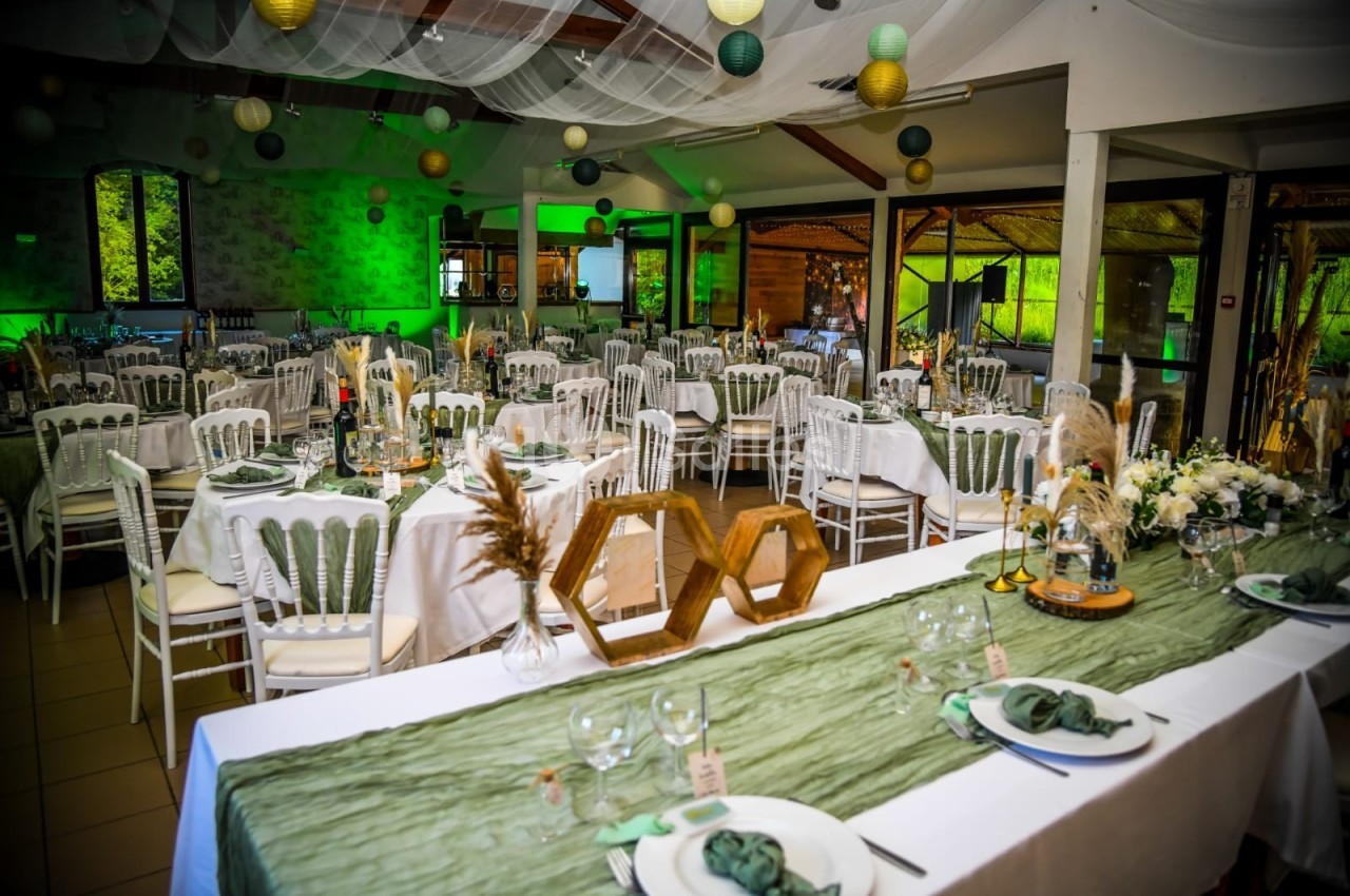 Salle de réception décorée pour un événement, avec tables dressées, nappes vertes et blanches, et suspensions colorées.