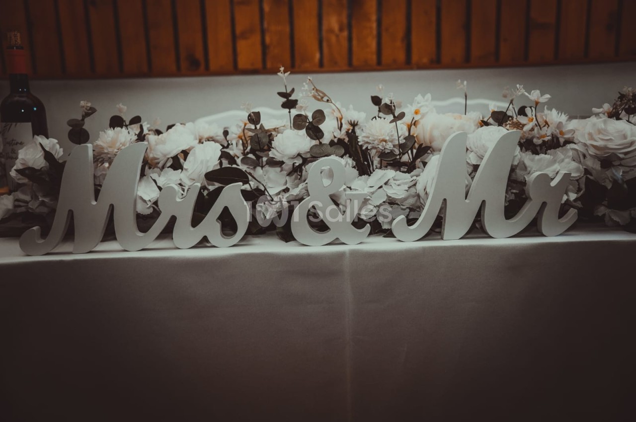 Décoration de table de mariage avec des lettres ’Mrs & Mr’ entourées de fleurs blanches et feuillages.