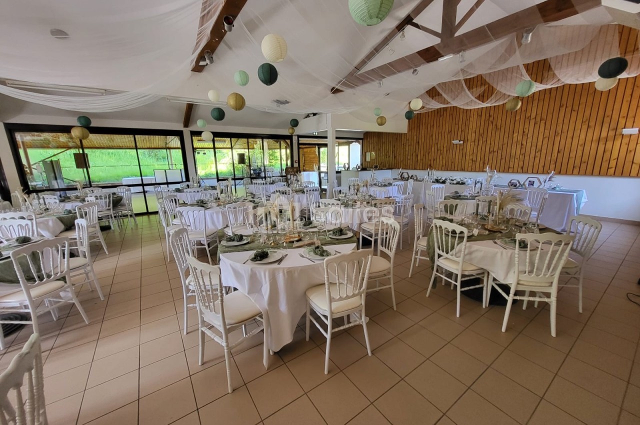 Salle de réception décorée avec des tables rondes dressées, des chaises blanches et des lanternes suspendues.