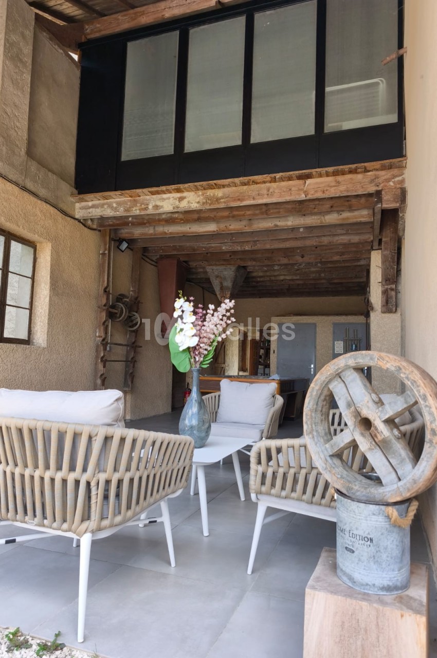 Espace extérieur couvert avec fauteuils en rotin, table basse, vase fleuri et éléments décoratifs rustiques.