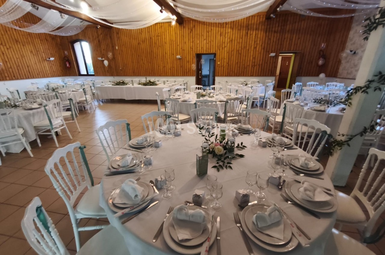Salle de réception décorée pour un mariage, avec tables rondes dressées, nappes blanches et compositions florales.