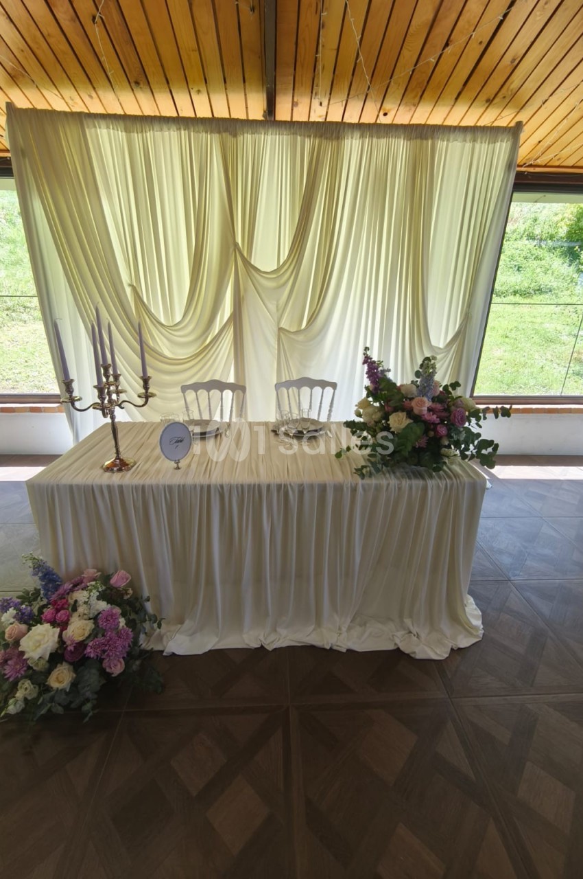 Table décorée pour un mariage avec nappes blanches, chandeliers, fleurs colorées et rideaux en arrière-plan.