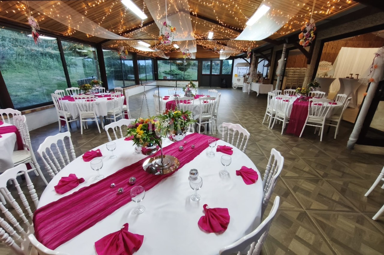Salle de réception décorée avec des tables rondes, nappes blanches, chemins de table roses et guirlandes lumineuses.