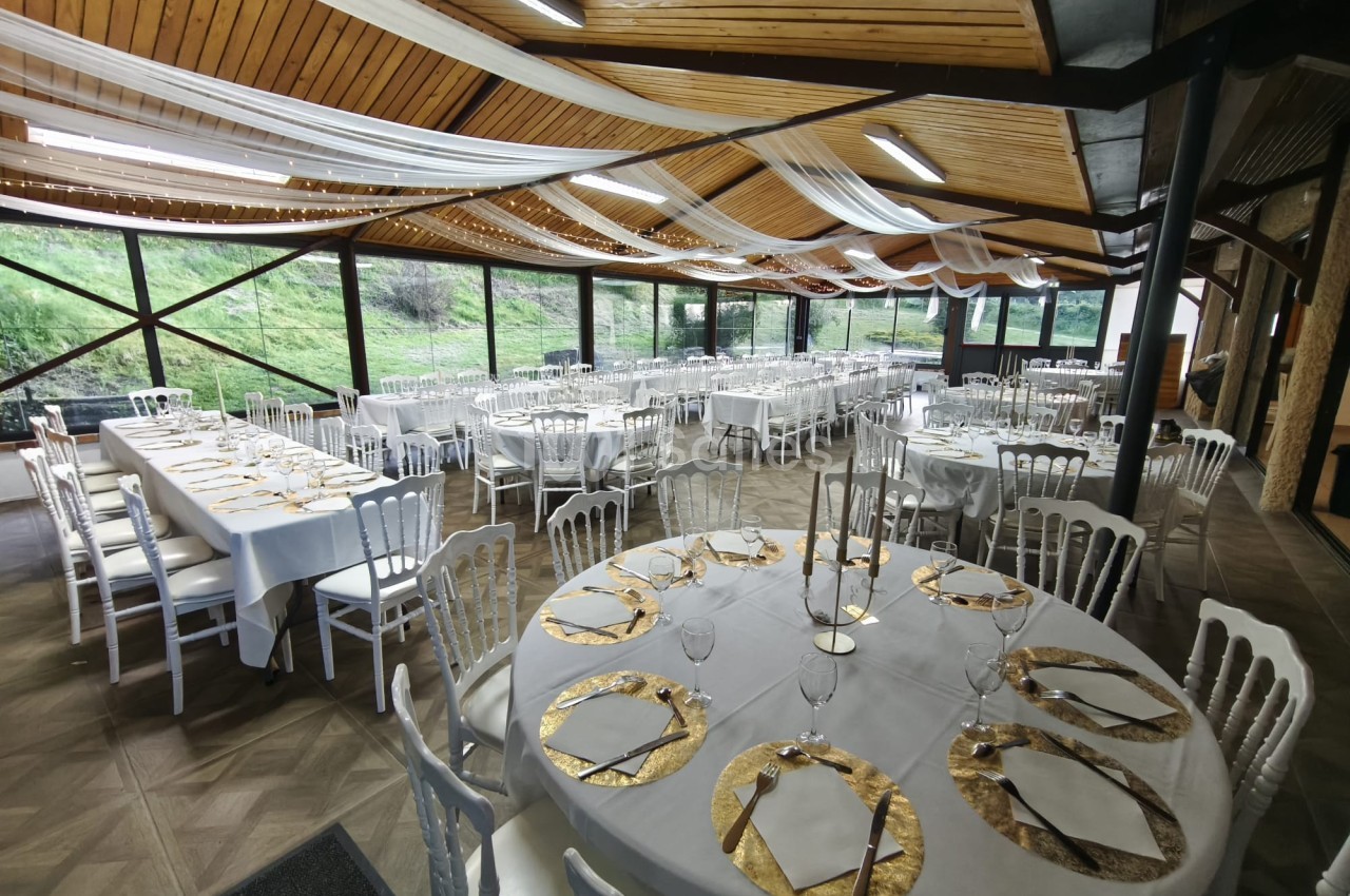 Salle de réception décorée avec des tables rondes et rectangulaires dressées, ornées de nappes blanches et détails dorés.