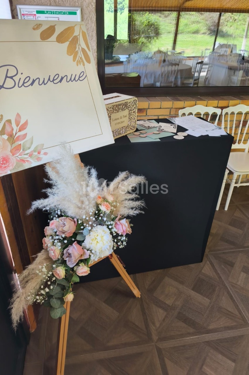 Panneau ’Bienvenue’ décoré de fleurs, posé sur un chevalet près d'une table d'accueil dans une salle lumineuse.