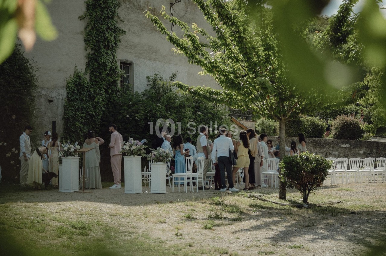 Groupe de personnes rassemblées dans un jardin, près de chaises blanches et de décorations florales.