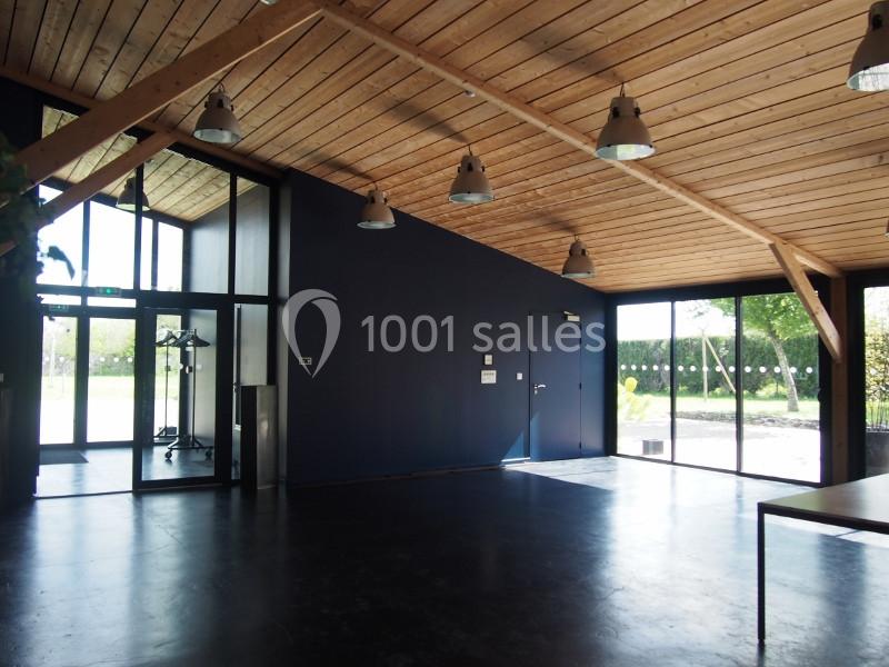 Salle lumineuse avec plafond en bois, murs sombres, sol noir, grandes fenêtres et vue sur un espace extérieur verdoyant.
