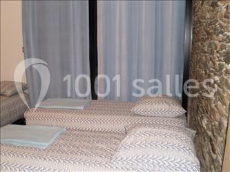 Deux lits simples avec draps à motifs géométriques, placés près d'un mur en pierre et devant des rideaux bleus.