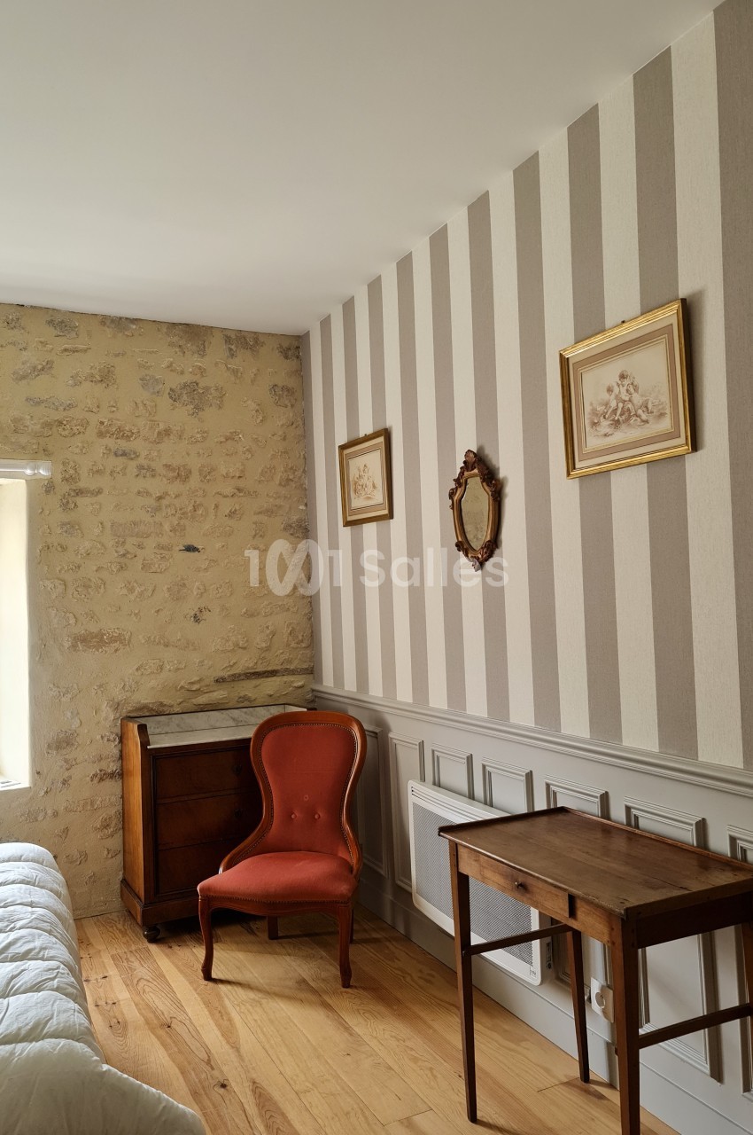Chambre avec mur en pierre et papier peint rayé, mobilier ancien comprenant une chaise, une table et un petit meuble.