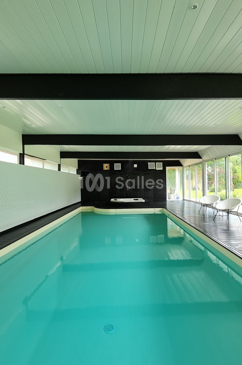 Piscine intérieure avec plafond en bois blanc, baies vitrées donnant sur un espace extérieur verdoyant.