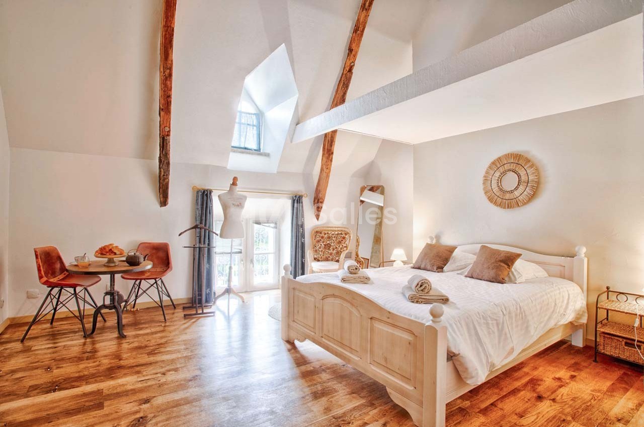 Chambre lumineuse avec lit double, parquet en bois, poutres apparentes, coin repas et décoration chaleureuse.