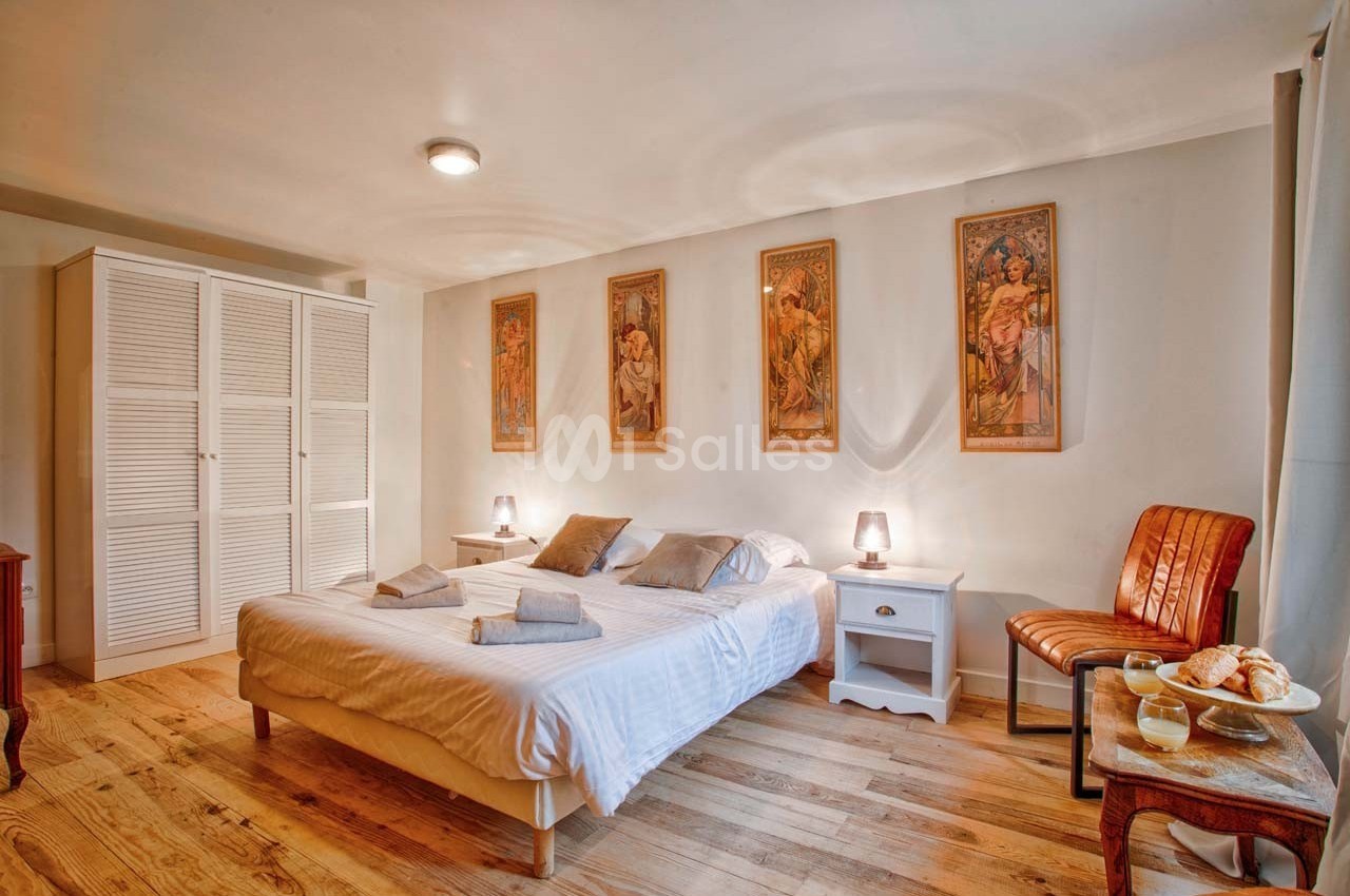 Chambre lumineuse avec lit double, parquet en bois, meubles simples et décorations murales artistiques.
