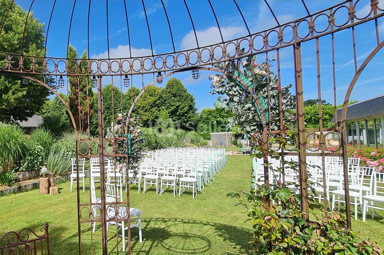 Chaises blanches alignées sur une pelouse sous une structure métallique, prêtes pour une cérémonie en plein air.
