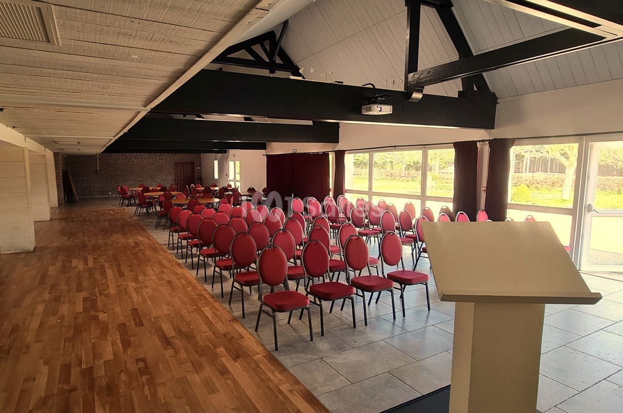 Salle de conférence lumineuse avec rangées de chaises rouges alignées face à un pupitre en bois clair.