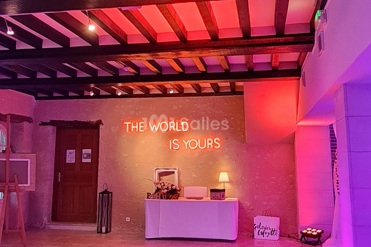 Salle éclairée par des lumières roses avec un néon ’The world is yours’ au mur, table décorative en dessous.
