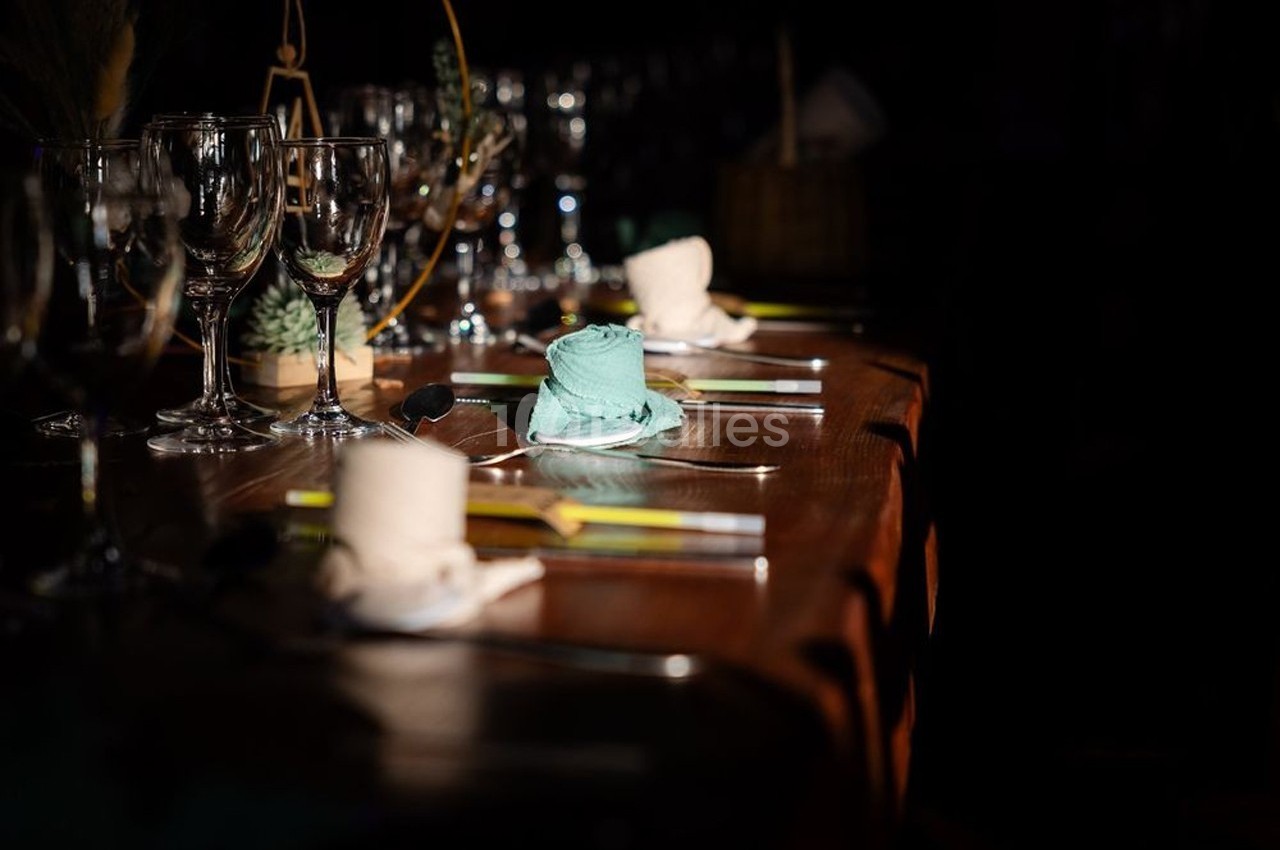 Table dressée avec des serviettes roulées, verres à pied et couverts, éclairée par une lumière tamisée.