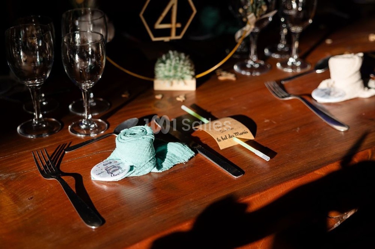 Table en bois dressée avec couverts, serviettes pliées, verres et une décoration de table comprenant un numéro 4.