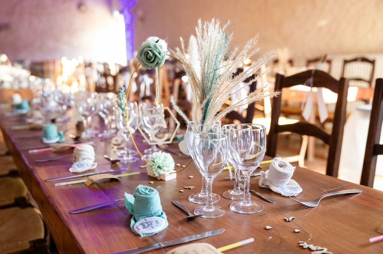 Table décorée pour un événement avec verres, couverts, serviettes pliées et ornements floraux dans une ambiance chaleureuse.