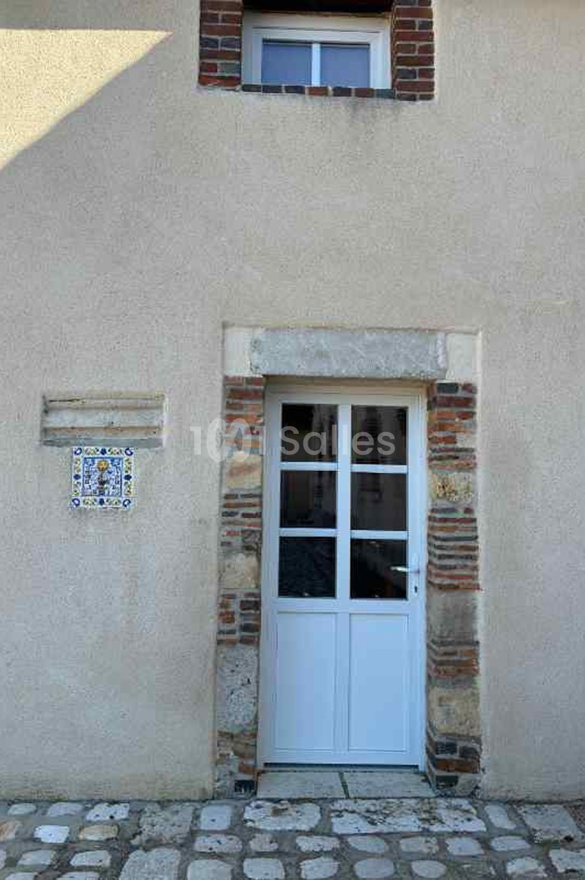 Porte blanche vitrée encadrée de briques et de pierres, avec une plaque décorative en céramique sur un mur beige.