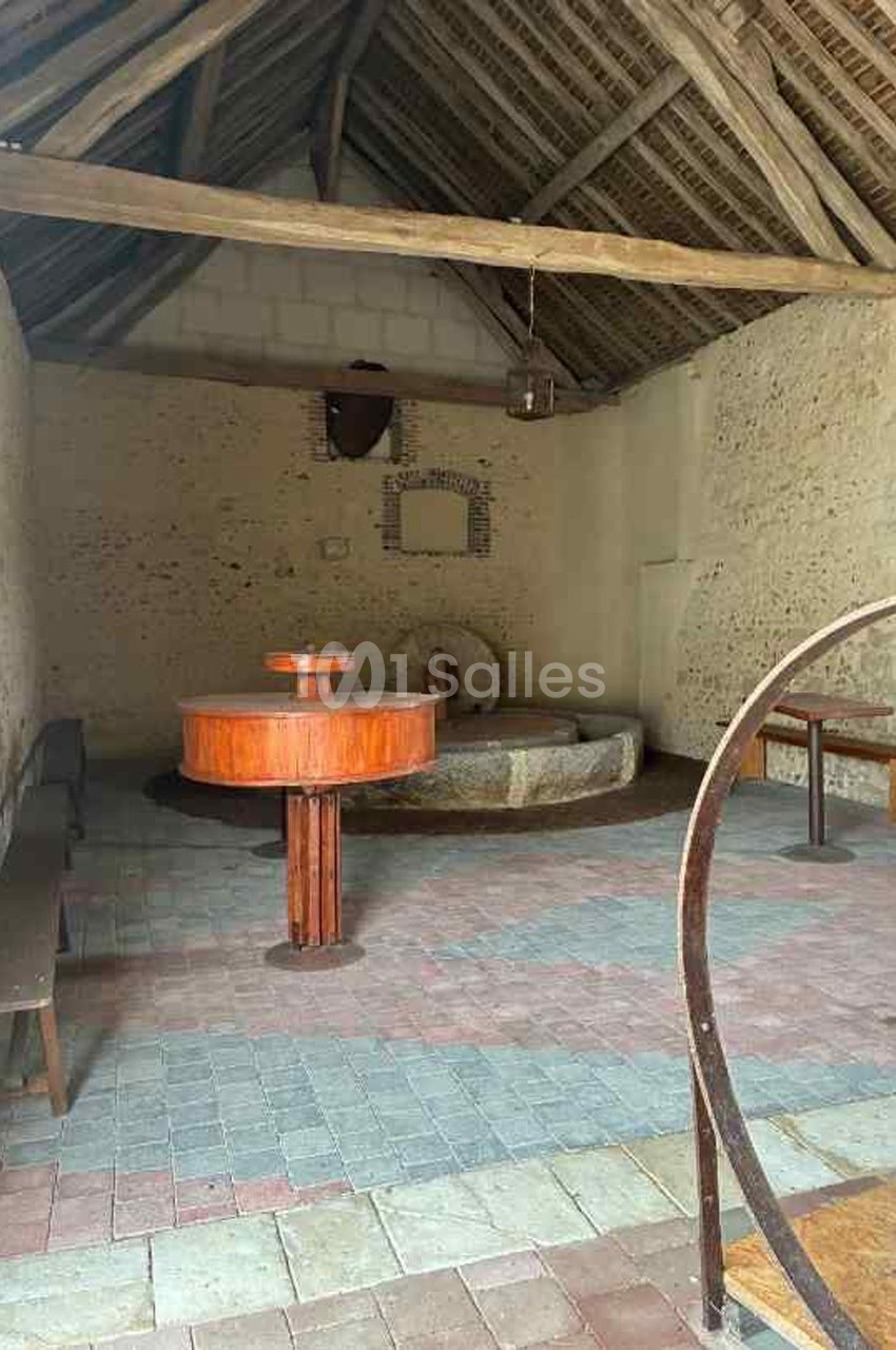 Intérieur d'une ancienne salle avec murs en pierre, toit en bois, bancs, et une cuve en pierre au centre.
