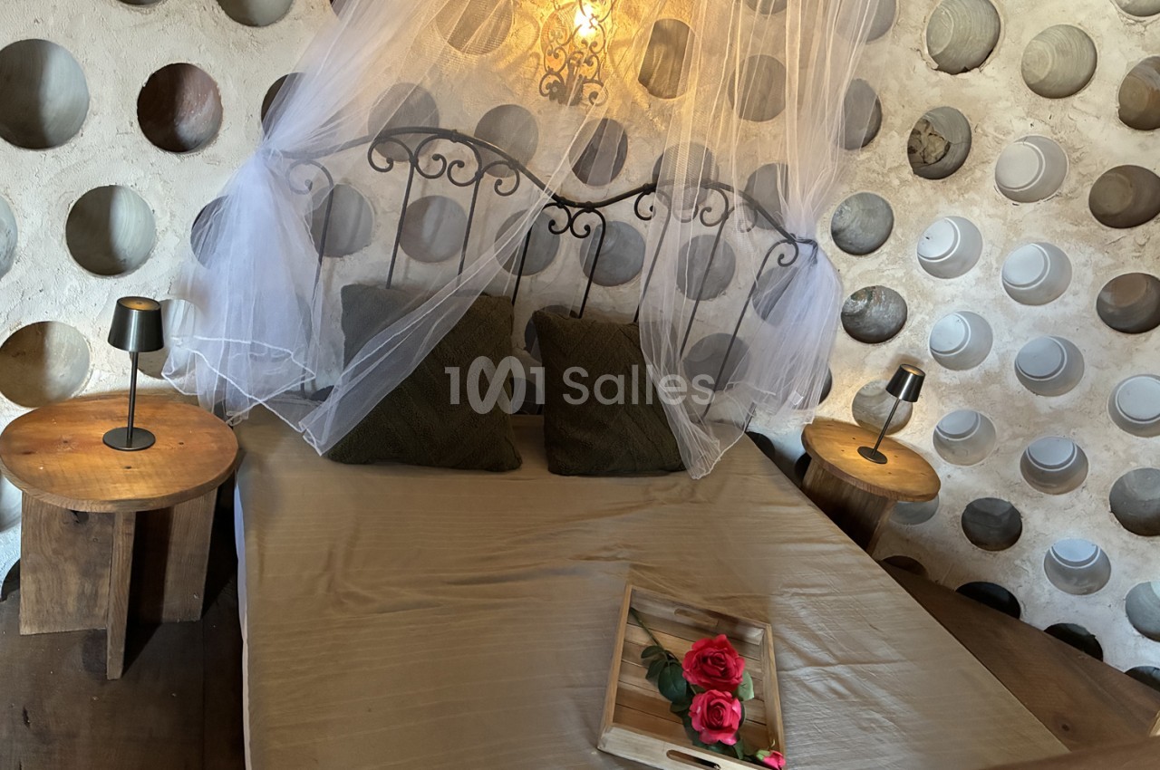 Lit dressé avec voile blanc, tête de lit en fer forgé, tables de nuit en bois et roses rouges - mur à niches décoratives.