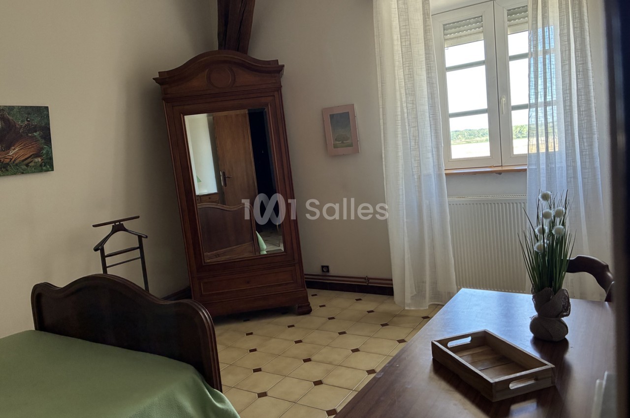 Chambre avec mobilier en bois massif, carrelage géométrique et larges fenêtres ouvertes sur la campagne.