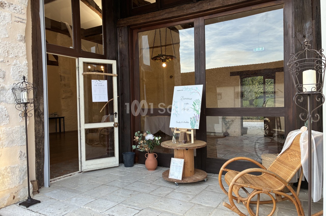 Entrée en pierre avec mobilier de rotin, affichage sur chevalet et vue sur cour intérieure.
