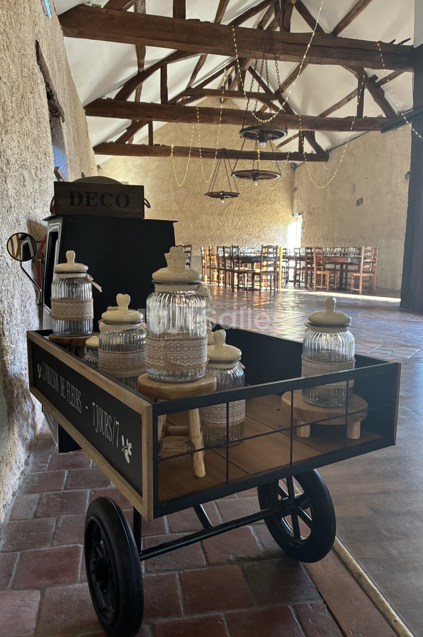 Chariot de décoration avec bocaux en verre et poutres apparentes dans salle aux chaises en paille.