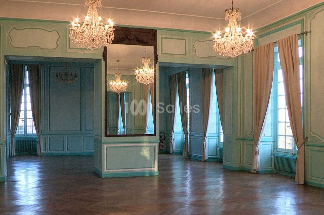 Salle élégante avec parquet en bois, murs bleu pastel, grands miroirs, lustres en cristal et hautes fenêtres avec rideaux.