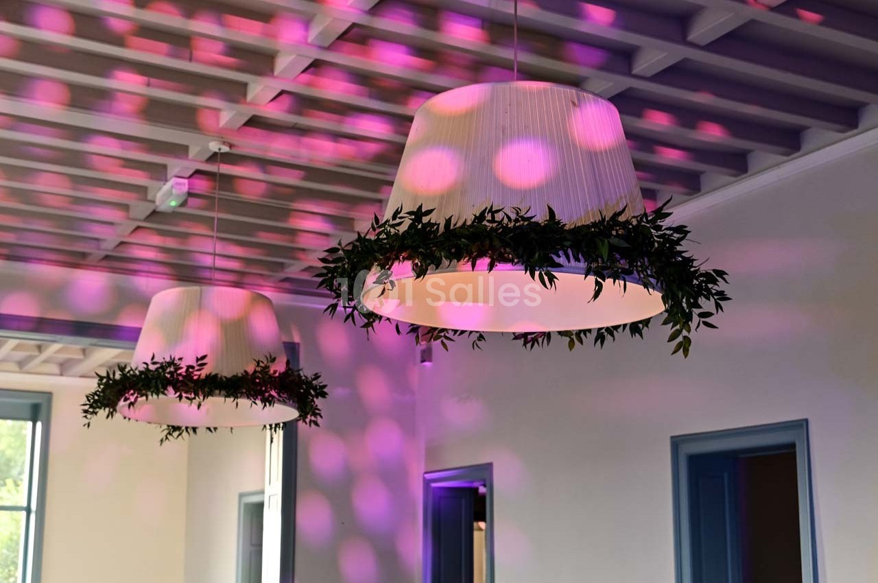 Deux suspensions décorées de feuillage, éclairées par des motifs lumineux roses dans une pièce lumineuse.