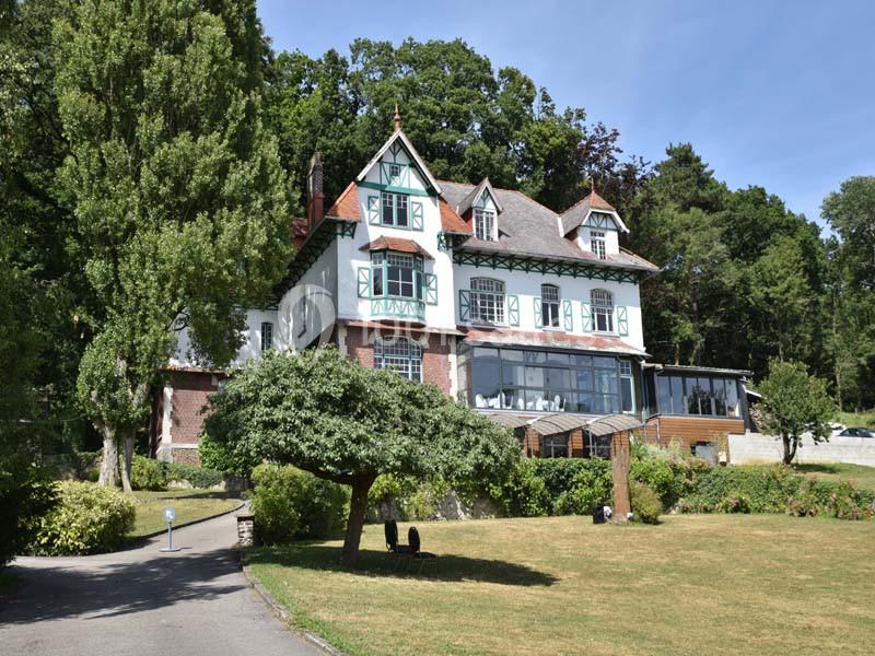 Grande maison de style traditionnel entourée d'arbres et d'une pelouse bien entretenue sous un ciel dégagé.